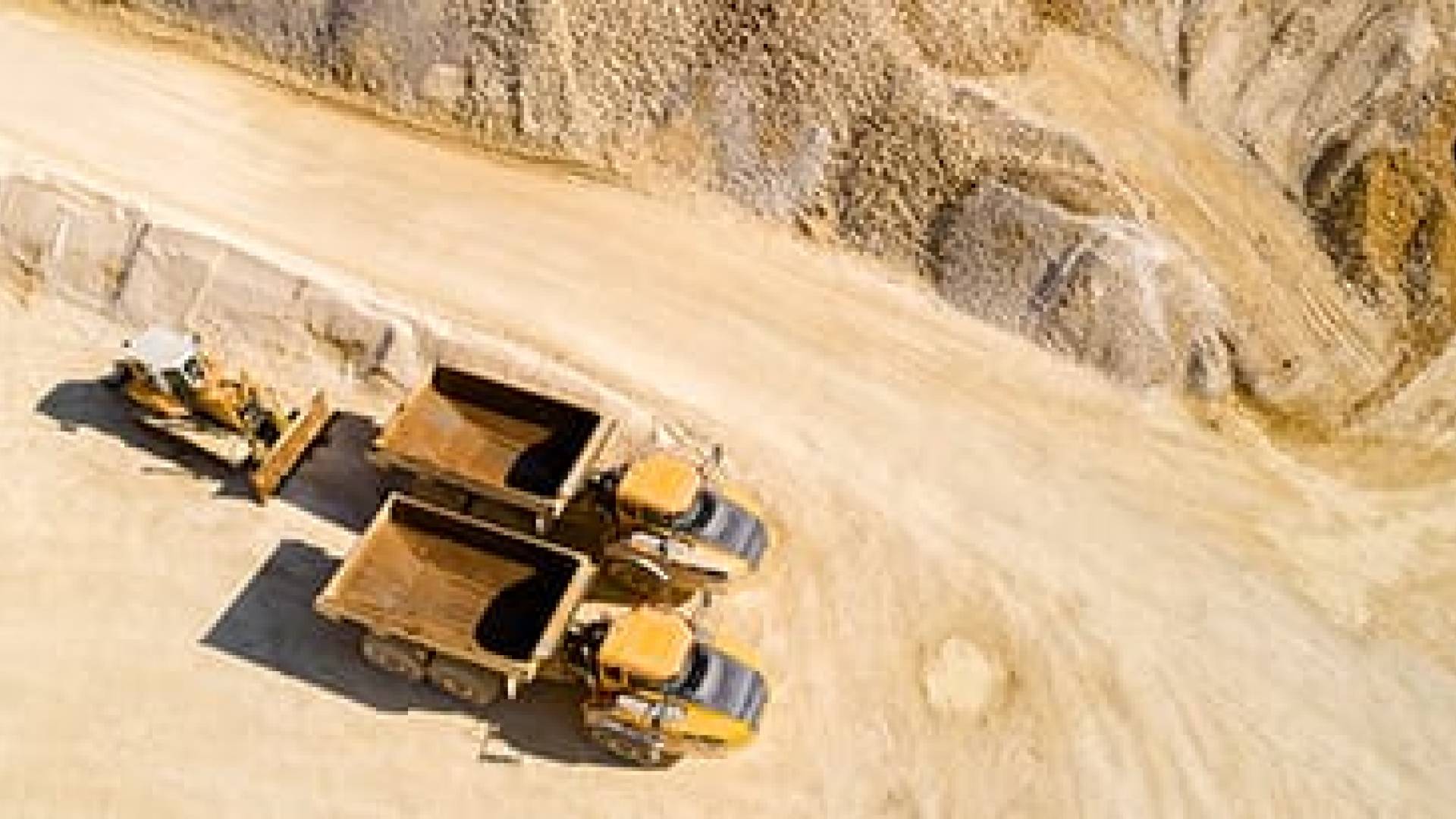 Aerial view of two dump trucks and a bulldozer in a quarry.