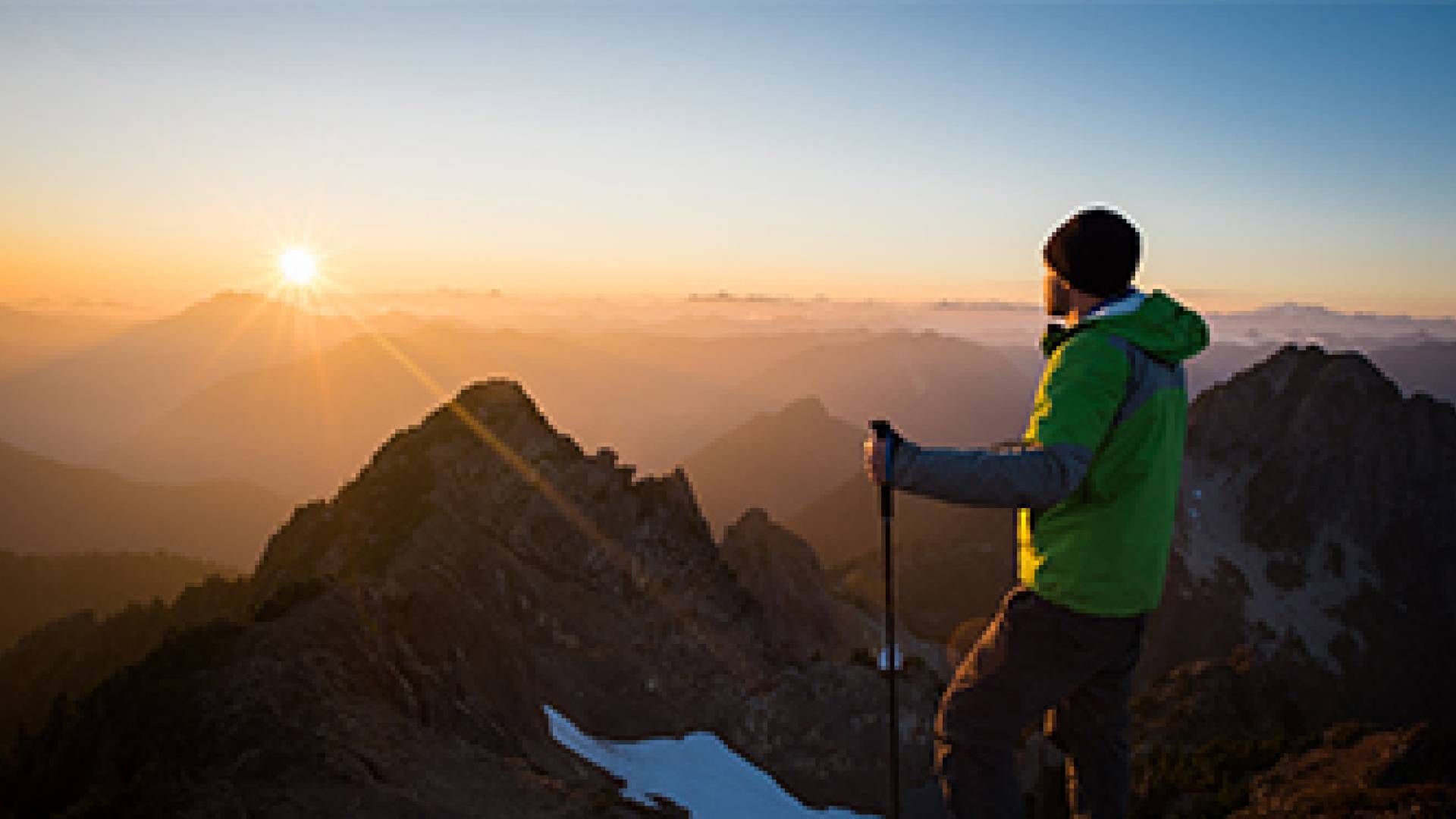 A hiker watching the sunrise on a mountain peak.