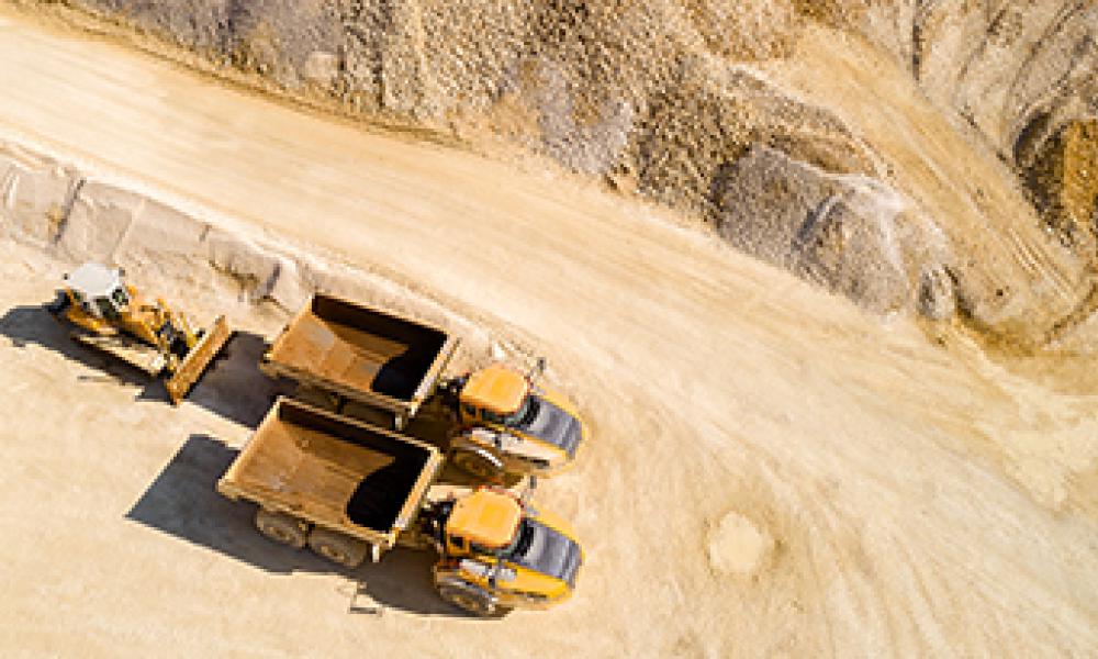 Aerial view of two dump trucks and a bulldozer in a quarry.
