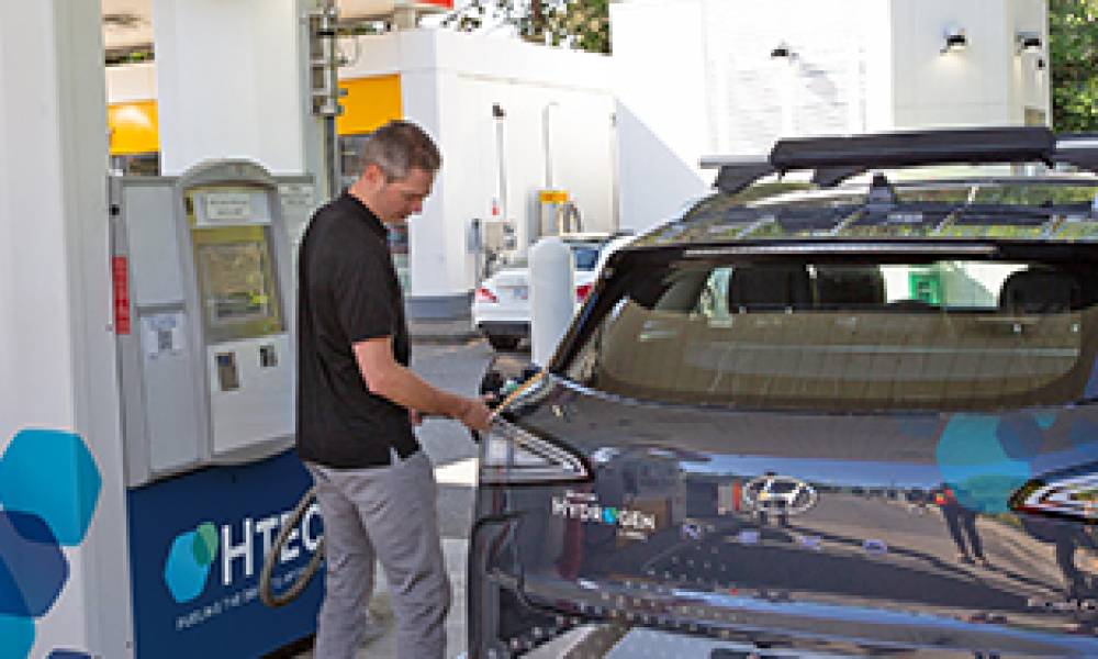 A man filling up a Hyundai Nexo hydrogen vehicle at a station.