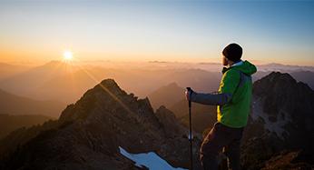 A hiker watching the sunrise on a mountain peak.